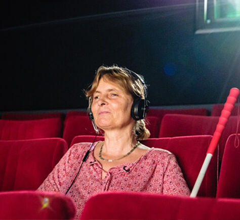 Kino Link führt zu allen Einträgen der Kategorie "Kino". Eine Frau mit Langstock sitzt im Kinosessel. Die Frau heißt Barbara Fickert und ist Kinoblindgängerin.